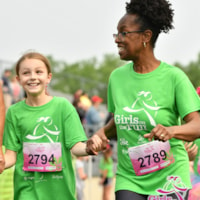 A Girls on the Run coach is smiling at kid wearing a green program shirt