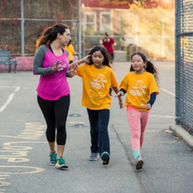 Girls on the Run coach walking with two girls in orange shirts.