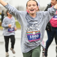 Girls on the Run participant with her arms up in the air smiling as she's running the 5K.