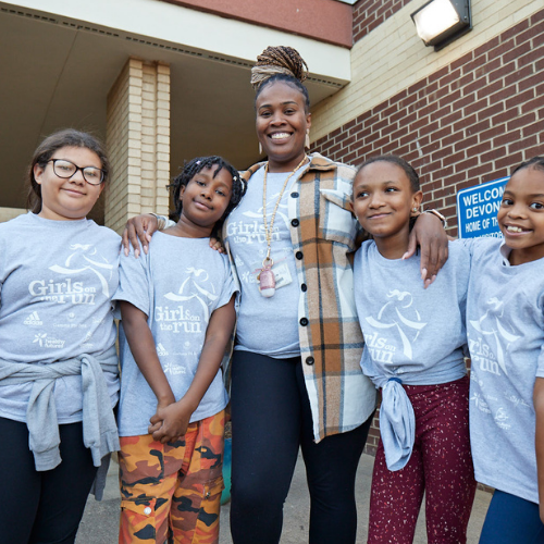 Four smiling girls and a Running Buddy wearing blue Girls on the Run t-shirts outdoors.
